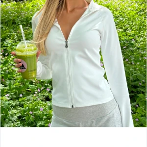 Vit träningsjacka med zip - Snygg och stilren vit jacka med dragkedja framtill. Jackan har en tight passform och långa ärmar, perfekt för en sportig look. Materialet är mjukt och stretchigt, vilket ger en bekväm känsla. Använd 1 gång så i princip som ny