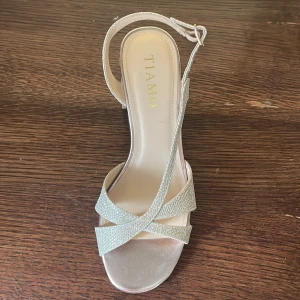 Glittriga sandaler från Tiamo - Snygga glittriga sandaler från Tiamo med öppen tå och klack. De har en elegant design med remmar som korsar över foten och en justerbar ankelrem. Använd en gång i fyra timmar. 899.- i nypris- nu 300.-