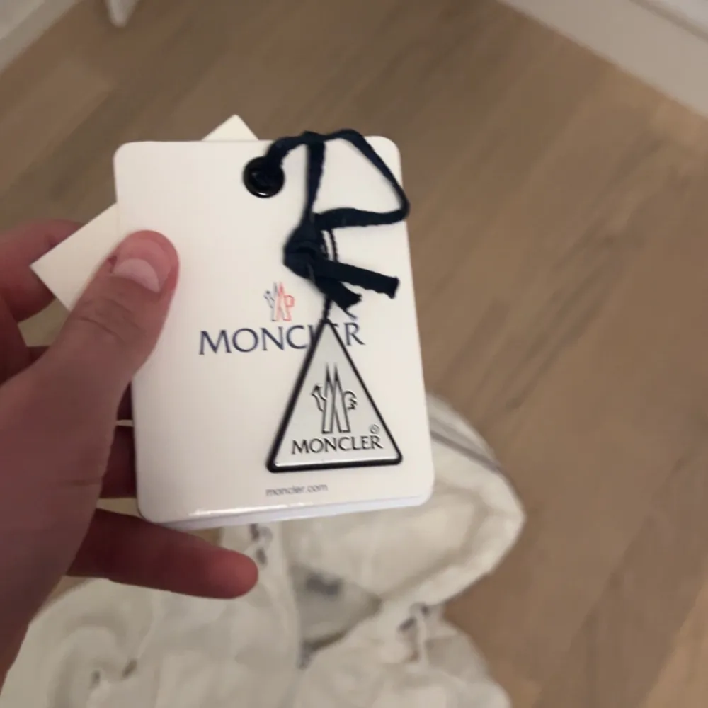 Säljer en snygg vit dunjacka från Moncler med huva och dragkedja. Jackan har långa ärmar och en quiltad design framtill. Perfekt för kyligare dagar! Liten fläck från svart ull. Takit.