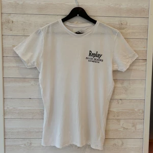 Vit t-shirt från Replay - Säljer en klassisk vit t-shirt från Replay med trycket 'Replay Blue Jeans Authentic' på bröstet. T-shirten har rund hals och är kortärmad, perfekt för en clean och enkel stil.