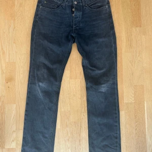 Svart jeans från Acne Studios - Säljer ett par mörkgrå jeans från Acne Studios med klassisk femficksdesign och raka ben. Jeansen har normal passform och stängs med knappgylf. Perfekta för dig som gillar stilrena och tidlösa jeans.
