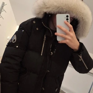 Svart dunjacka med päls från Moose Knuckles - Säljer en sjukt fet svart dunjacka från Moose Knuckles med stor luva med äkta fjällrävspäls. Jackan har flera fickor med dragkedja och knappar. Perfekt för kalla dagar med dens tjocka och varma design. Priset kan diskuteras men inte överdrivet.