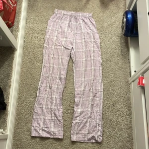 Lila rutiga byxor från Gina Tricot - Säljer ett par bekväma lila rutiga byxor från Gina Tricot. Byxorna har en elastisk midja och är perfekta för en avslappnad stil. De är tillverkade i ett mjukt material som känns skönt mot huden.