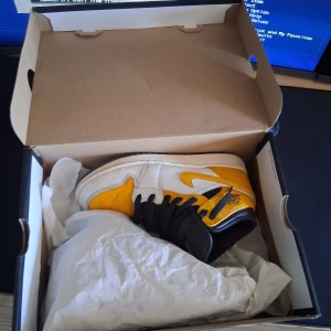 Jordan 1 - Snygga Nike Air Jordans i en fräsch kombination av gult, vitt och svart. Skorna har den klassiska Air Jordan-loggan på sidan och svart snörning. Perfekta för att ge din outfit en sportig touch. I stl 36