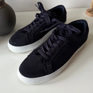 Marinblåa les deux skor - Snygga marinblåa sneakers i mocka från Les Deux med vita sulor och snörning. Diskreta broderade detaljer i rött och blått på hälen ger en stilren touch. Perfekta för en avslappnad look. Storlek 42. De är i mycket bra skick. 
