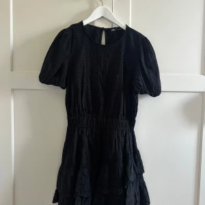 Svart klänning från Zara - Snygg svart klänning från Zara med korta puffärmar och volangdetaljer. Klänningen har en rund halsringning och en elastisk midja för en bekväm passform. Perfekt för en stilren look.