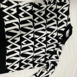 Svartvit mönstrad tröja från Moncler - Säljer en svartvit tröja från Moncler med grafiskt, zigzag-liknande mönster. Tröjan är långärmad och tillverkad i bomull, med ribbade muddar vid ärmslut och nederkant. Perfekt för dig som gillar statement-plagg!