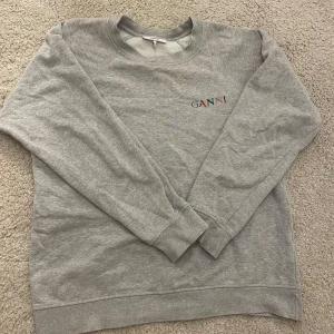 Ganni sweatshirt  - Säljer en grå sweatshirt från Ganni med broderad logga i flera färger på bröstet. Tröjan har rund halsringning och långa ärmar. Perfekt för en avslappnad och stilren look. Använt fåtal gånger. Skulle säga att den passar storlek s och m. Pris kan diskuteras💕