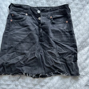 Svart jeanskjol med rå kant - Snygg svart jeanskjol med rå kant och knappdetaljer fram. Kjolen har fickor både fram och bak, vilket ger en cool och avslappnad look. Perfekt för en casual outfit.