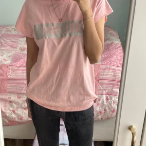 Rosa t-shirt med tryck från Firefly - Säljer en ljusrosa t-shirt från Firefly med texten 'GRL PWR' tryckt på bröstet i vitt och ljusgrått. T-shirten har korta ärmar och en klassisk rund halsringning. Perfekt för dig som gillar enkel och snygg stil.