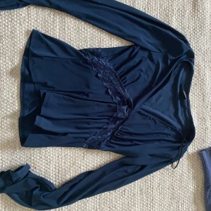 Svart omlottopp med spets från Gina Tricot - Säljer en svart omlottopp från Gina Tricot med långa ärmar och fina spetsdetaljer längs omlottringningen. Toppens material är mjukt och stretchigt, perfekt för en stilren look. Köpte runt jul men säljer då de inte kommer till användning. Köparen står för frakt om vi inte kommer överens om annat❤️
