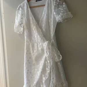 Vit omlottklänning med spetsdetaljer - Superfin vit omlottklänning med blommigt spetsmönster från Gina tricot. Perfekt till skolavslutning eller student☺️Använd endast en gång