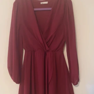 Vinröd omlottklänning  och svart klänning - Vinröd klänning med omlott-skärning och långa ärmar. Klänningen har markerad midja och ett mjukt, flytande tyg som ger ett elegant fall. Perfekt för dig som gillar en klassisk och feminin stil. Båda har storlek 36, kan sälja tillsammans eller enskilt. 150kr var eller 250kr båda