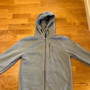 Sail Racing - Ljusblå hoodie från Sail Racing, tröjan har två fickor och logga på bröstet samt på huvan. Hör av dig vid frågor.