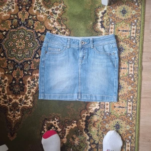 Ljusblå jeanskjol med klassiska fickor - Säljer en ljusblå jeanskjol från Lindex med klassisk femficksdesign och knappgylf. Kjolen har bälteshällor och är sydd i ett mjukt denimtyg. Perfekt för dig som gillar en enkel och tidlös stil.
