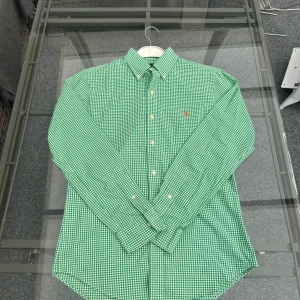 Ralph Lauren Slim Fit Skjorta - Small - (ÖPPEN FÖR BUD)                                                                             Säljer en superfin Ralph Lauren slim fit skjorta i storlek S. Färgen är grön med ett vitt småmönstrat rutmönster och klassisk röd logga på bröstet. Modellen är slim fit och sitter riktigt snyggt på kroppen. Använd några gånger jätte fint skick. Perfekt till både vardag och fest!  Storlek: S Färg: Grön/Vit rutmönstrad Passform: Slim fit Pris: 499kr  Frakt eller mötas upp i Jönköping 