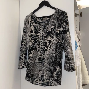 Svartvit mönstrad blus från Vero Moda - Säljer en svartvit blus från Vero Moda med abstrakt mönster. Blusen har v-ringning och trekvartsärm, perfekt för dig som gillar unika prints. Lätt och skönt material som passar till många tillfällen. 