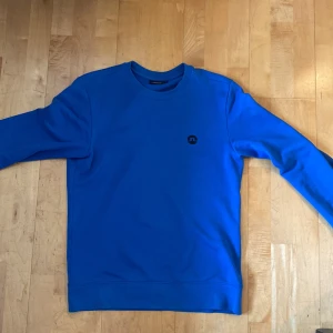 Blå sweatshirt från J.Lindeberg - Säljer en stilren blå sweatshirt från J.Lindeberg.  Perfekt för vardags bärande och golf. 