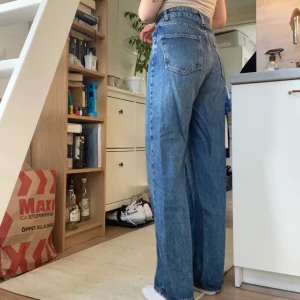 Blå raka jeans med hög midja - Säljer ett par klassiska blå jeans från Gina i storlek 36 med hög midja och raka, vida ben. Dem är i bra skick, möjligtvis lite lite slitna längst ned vid slutet av byxorna men inget märkbart!