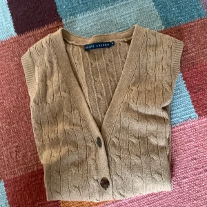 Beige stickad väst från Ralph Lauren - Säljer en beige stickad väst från Ralph Lauren med klassiskt kabelstickat mönster och v-ringning. Västen har knappar framtill och är ärmlös, perfekt för lager-på-lager-stil. Du kan se att varan är äkta på 2 o 3 bilden! Fråga gärna allmäna frågor eller prisförslag!!