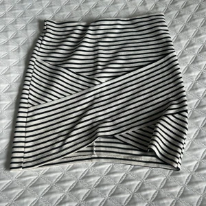 Svartvit randig kjol - Säljer en svartvit randig kortkjol med horisontella och diagonala ränder. Kjolen är figurnära och har en enkel, stilren design utan extra detaljer. Perfekt för dig som gillar klassiska mönster och vill ha en bekväm kjol till vardags.