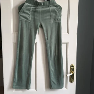 Gröna mjukisbyxor från Juicy Couture - Snygga ljusgröna mjukisbyxor från Juicy Couture med broderad logga på ena benet. Byxorna har normal passform, dragsko i midjan och stora fickor fram och bak. Perfekta för en avslappnad och trendig look.
