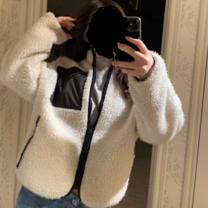 Vit teddyjacka med svarta detaljer - Mysig vit teddyjacka med svarta detaljer och dragkedja framtill. Jackan har en svart bröstficka och är långärmad med en avslappnad passform. Storlek xxs men passar även xs, s och m. Jag är ca 160cm