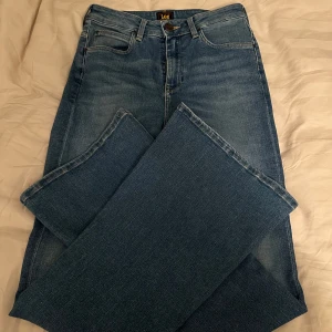 Blå jeansbyxor från Lee - Säljer ett par klassiska blå jeans från Lee med fem fickor och normal passform. Byxorna har bootcut ben och traditionell knappgylf dom är även hög midjade. Perfekta till vardags för en avslappnad stil. Stolek W28 L31
