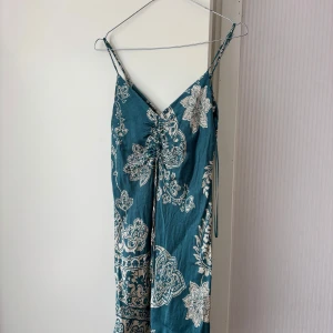 Blå mönstrad klänning med knyt från Zara - Säljer en blå klänning från Zara med vitt blommigt mönster och smala axelband. Klänningen har v-ringning och knytning framtill som ger en snygg detalj. Passar mig som bär S/M. Tveka inte på att höra av dig vid frågor eller prisförslag!