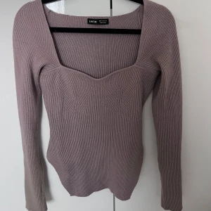 Ljuslila ribbad topp med fyrkantig ringning från SHEIN - Trendig ljuslila ribbad topp från SHEIN med lång ärm och snygg fyrkantig ringning. Toppen har en figurnära passform och subtila stickade detaljer framtill. Perfekt att styla till jeans eller kjol.