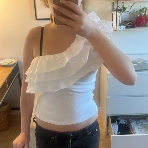 Vit one shoulder topp med volang från Zara - Säljer min vita topp från zara då den inte kommer till användning. använt den en gång. skriv för frågor eller fler bilder💕 använd gärna köp nu. 