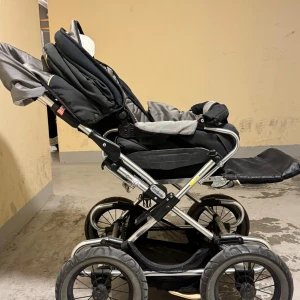 Svart och grå barnvagn från Emmaljunga - Säljer en svart och grå barnvagn från Emmaljunga med robust ram i metall och stora hjul. Vagnen har justerbart ryggstöd, fotstöd och en praktisk varukorg undertill. Perfekt för promenader i stan eller i parken.