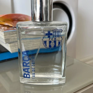 Barca Eau de Toilette herrparfym - Fräsch herrparfym i glasflaska med FC Barcelonas logga och silverfärgad kork. Doften är sportig och flaskan har en stilren, rektangulär form. Perfekt för dig som gillar fotboll och vill ha en unik doft i samlingen.