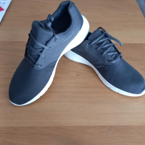 Mörkgrå sneakers med vit sula - Snygga mörkgrå sneakers med vit, platt sula och rund tå. Skorna har snörning och är tillverkade i syntetmaterial med mesh-liknande ovandel. Perfekta för vardagsbruk eller träning. Säljer för 350:-             NY pris 499:-   Priset Kan diskuteras. 
