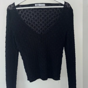 Svart stickad spets topp  - Säljer en svart stickad topp från Zara med v-ringning och lång ärm. Tröjan har ett diskret mönster i tyget som ger en snygg struktur. Perfekt att styla med jeans eller kjol.