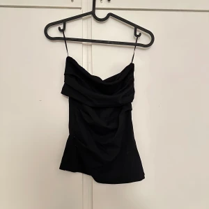 Svart draperad tubtopp - Säljer en svart tubtopp och snygg drapering framtill. Perfekt för dig som vill ha en stilren och trendig topp till sommaren.