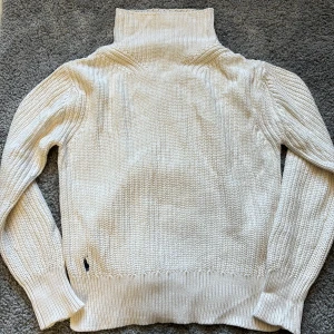 Vit stickad polotröja från Polo Ralph Lauren - Säljer en klassisk vit stickad polotröja från Polo Ralph Lauren. Tröjan har hög polokrage, lång ärm och ribbade muddar. Perfekt för lager-på-lager och en stilren look.