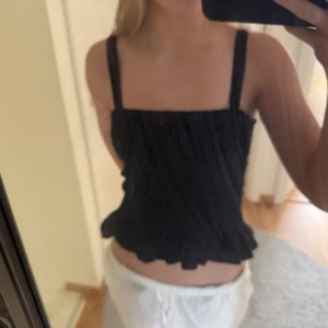 Svart smockad linnetopp från H&M - Säljer en svart smockad linnetopp från H&M med breda axelband. Toppen är elastisk och sitter tight mot kroppen, perfekt för sommardagar. Enkel och stilren design som passar till mycket.