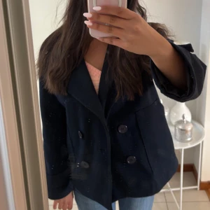 Designbysi kappa - Säljer en extremt fin mörkblå designbysi kappa med dubbelknäppning. Jackan har lång ärm och en rak passform som ger en stilren look. Perfekt att slänga på sig överh en hoodie eller tröja.