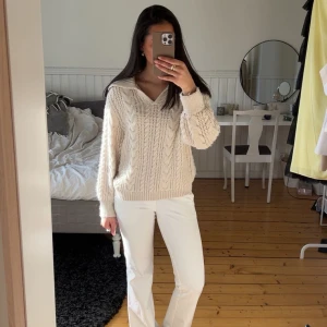 Beige stickad kabelmönstrad tröja med krage - Säljer en beige stickad tröja med kabelmönster och v-ringning. Tröjan har en bred krage och långa ärmar med ribbade muddar.🤍