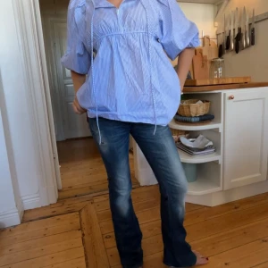 Blå bootcut jeans med slitningar - Snygga blå jeans med bootcut passform och låg midja. Jeansen har slitna detaljer och en klassisk femficksdesign med knappgylf. Perfekta till vardags för en avslappnad stil.