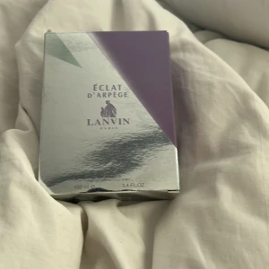 Éclat d'Arpège Eau de Parfum från Lanvin - Säljer en 100 ml flaska Éclat d'Arpège Eau de Parfum från Lanvin. Parfymen kommer i en elegant, genomskinlig glasflaska med vit kork och har en stilren, silvrig förpackning med lila detaljer. En klassisk och feminin doft från ett välkänt franskt märke.