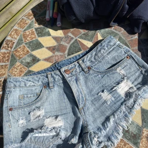 Ljusa lågmidjade jeansshorts med fransar  - Snygga ljusblå jeansshorts från Divided med slitna detaljer och fransig kant. Klassisk femficksmodell med knapp och dragkedja framtill. Perfekta för varma dagar och en avslappnad stil. Lågmidjade men tyvärr för små för mig