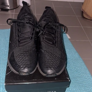 Svarta Nike Air Max 270 sneakers - Säljer ett par helsvarta Nike Air Max 270 sneakers med synlig Air Max-dämpning i hälen. Skorna har stickad ovandel i syntetmaterial och klassisk snörning. Perfekta för dig som gillar sportig och stilren look. Kommer inte med originell box 