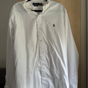 Vit skjorta från Polo Ralph Lauren - Klassisk vit skjorta från Polo Ralph Lauren i custom fit. Skjortan har lång ärm, knappar framtill och den ikoniska broderade loggan på bröstet. Perfekt till många olika stilar och tillfällen. CUSTOM FIT STRETCH OXFORD SHIRT WHITE  Säljer för den är för stor.  Nypris: 1795,00kr