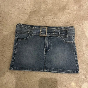 Lågmidjad mini jeans kjol med bälte - Snygg jeanskjol i ljusblå färg och ett bälte som går att ta av. Kjolen ser mörkare ut på bild än i verkligheten, utan den är mer jeans-ljusblå i verkligheten. (se sista bilden) Lågmidjad, kort. Storlek S passar XS Midjemått: 38 cm rakt över Längd: 27m