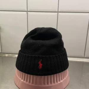 Svart mössa från Polo Ralph Lauren - Snygg svart mössa från Polo Ralph Lauren med röd broderad logga framtill. Skick 8/10. Onesize. Hör av er vid funderingar!