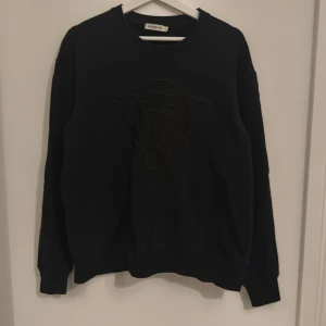 Svart tröja från Tiger of Sweden - Säljer en stilren svart tröja från Tiger of Sweden med ett diskret broderat mönster på framsidan. Tröjan har långa ärmar och en rund halsringning. Perfekt för en minimalistisk look. 