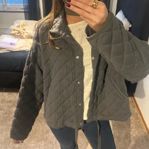 Grå quiltad jacka - Säljer en snygg grå quiltad jacka med knappar och dragsko i nederkant. Jackan har en avslappnad passform och långa ärmar, perfekt för kyligare dagar. Och passar perfekt intill våren och sommaren❣️