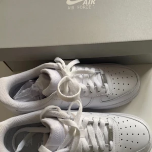 Vita Nike Air Force 1 - Säljer ett par nya klassiska vita Nike Air Force 1 sneakers. De har en stilren design med snörning och perforerade detaljer på ovansidan för ventilation. Perfekta för en casual look. De är aldrig använda !! Säljer eftersom att jag aldrig hann lämna tillbaka dem, därav priset. skriv gärna om du har frågor !!
